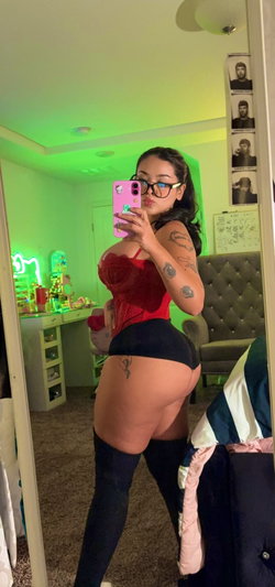 Woman in red corset taking mirror selfie in bedroom.