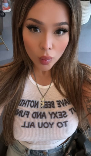 Woman with long brown hair in white top taking selfie indoors.