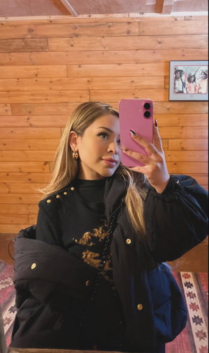 Woman with blonde hair taking mirror selfie in black jacket.