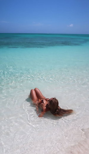 Woman in bikini lying in shallow turquoise water at beach.