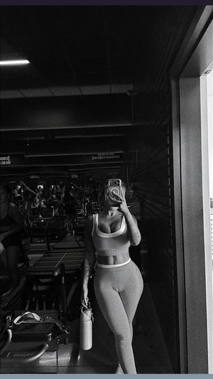 Woman in form-fitting gym outfit takes mirror selfie in dark gym.
