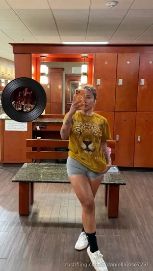 Woman in yellow tiger tee and gray shorts poses in gym locker room mirror selfie.