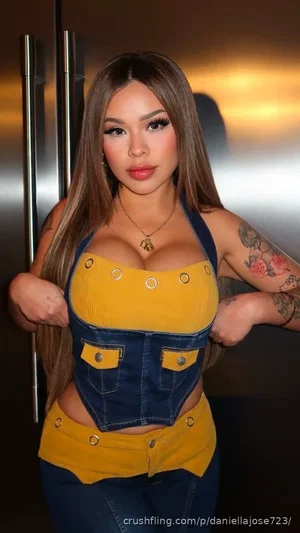 Woman with long brown hair and tattoos wearing a yellow and denim crop top and jeans, standing