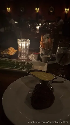 Dinner table with steak, asparagus, fries, and candlelight in a dimly lit restaurant.