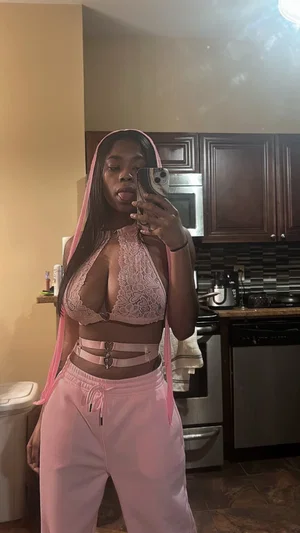 Woman in pink lace top and sweatpants taking mirror selfie in kitchen.