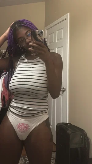 Woman with purple braids in striped tank top and white underwear, taking mirror selfie indoors.