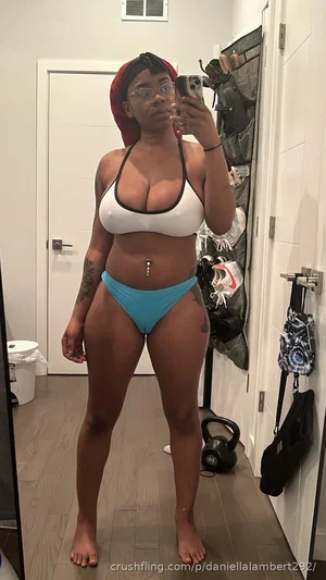 Woman in white bikini top and blue bottoms, wearing red headwrap, taking mirror selfie in indoor