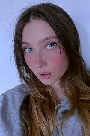 Woman with long brown hair and freckles wearing grey hoodie indoors.