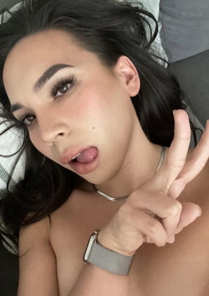 Woman with dark hair lying down, bare shoulders, making peace sign, wearing silver necklace and