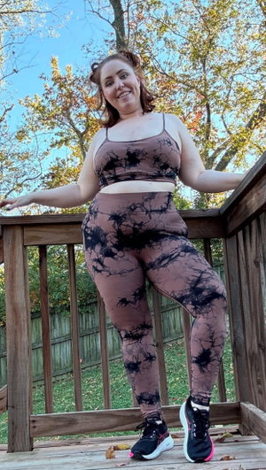 Woman in patterned sports bra and leggings posing on wooden deck outdoors.
