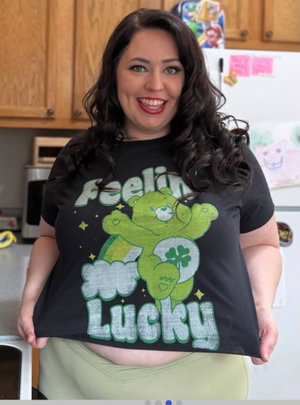 Woman with dark curly hair wearing black graphic tee and light green pants in kitchen.
