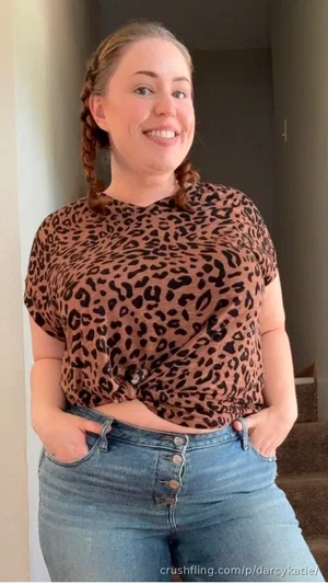 Woman with braided hair in leopard print top and jeans, standing indoors.