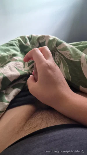Person under green patterned blanket, hand near lower abdomen, wearing dark clothing.