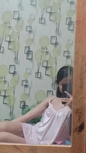 Woman in white dress taking mirror selfie indoors.