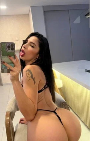 Woman with long black hair taking selfie in kitchen wearing black lingerie.