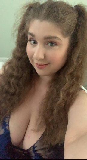 Woman with curly brown hair in blue lingerie taking selfie indoors.