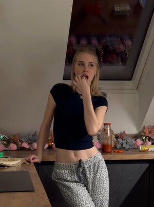 Blonde woman in black crop top and leopard pants in kitchen.