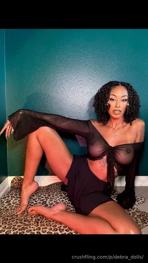Woman in black sheer top and shorts posing on leopard print rug against teal wall.