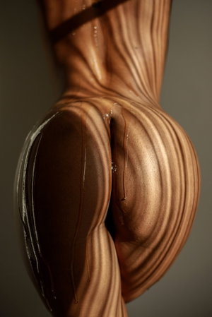 Athletic person with glossy skin and dark straps in studio.
