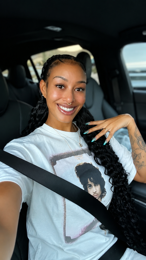 Smiling woman with braided hair in white t-shirt inside car.