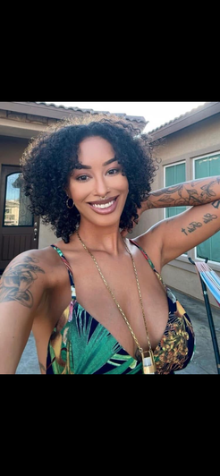 Woman with curly hair in colorful top taking outdoor selfie.