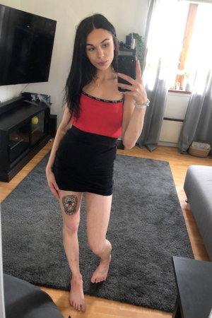 Slim woman in red top and black mini skirt indoors.