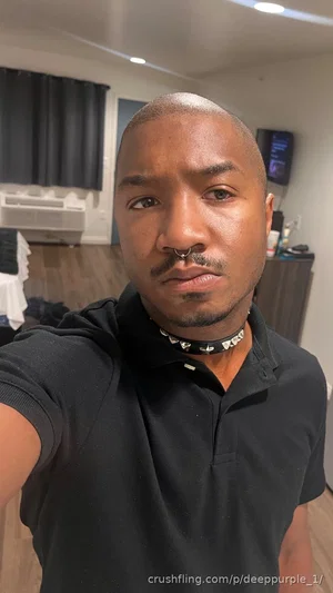 Man with shaved head and nose ring wearing black polo shirt in indoor room.