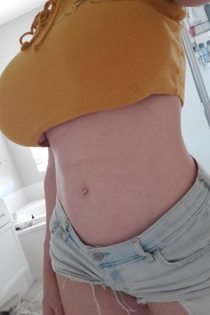 Curvy woman in yellow crop top and denim shorts in bathroom.
