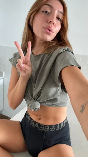 Woman in olive crop top and black shorts posing with peace sign indoors.