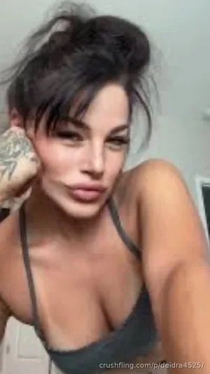 Woman with dark hair in a messy bun, wearing a gray bra, posing indoors.