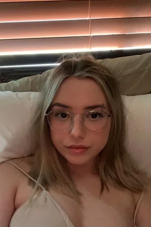 Blonde woman in glasses and strap top on bed.
