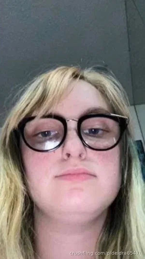 Blonde woman with round glasses in a close-up indoor selfie.