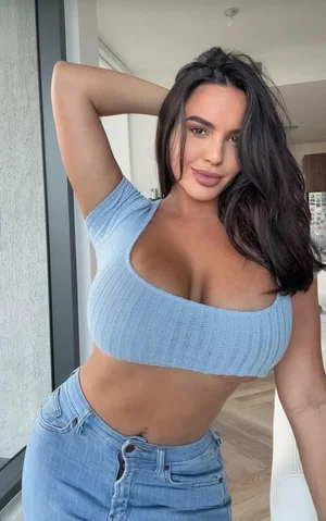 Curvy woman in blue crop top and jeans indoors.