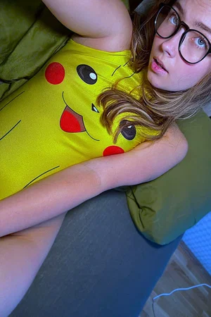 Woman with glasses in Pikachu shirt on bed.