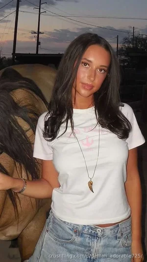 Woman with long dark hair in white t-shirt and jeans, standing outdoors at dusk.