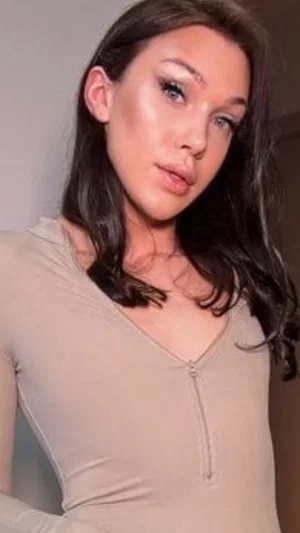 Woman with long dark hair in a beige zip-front top, indoors.