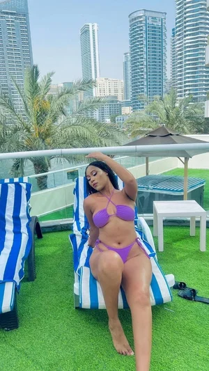Woman in purple bikini lounging on striped chair on rooftop with city skyline.