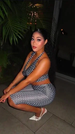 Woman in polka dot two-piece outfit crouching outdoors at night near plants.