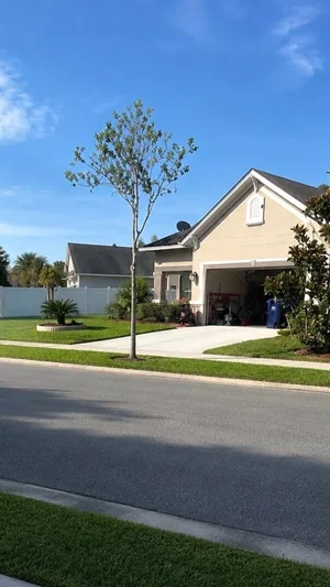Suburban house with beige exterior, garage, and front yard under clear blue sky.