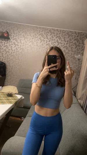 Woman in blue crop top and leggings takes mirror selfie in living room.