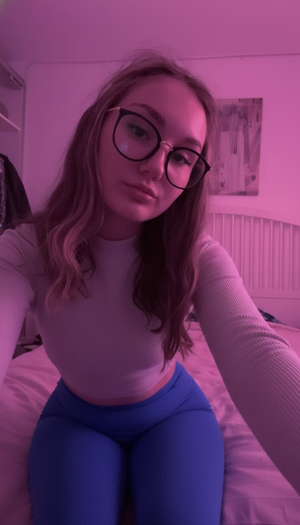 Woman with glasses in gray top and blue leggings on bed.