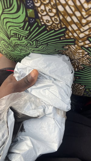 Dark-skinned hand holding white bags on green-gold fabric.
