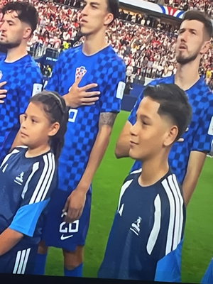 Adult men and children in blue soccer jerseys standing on a field during a ceremony.