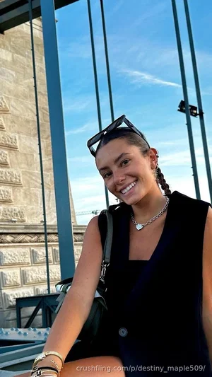 Woman in black sleeveless top, smiling, outdoors near stone building with metal beams.