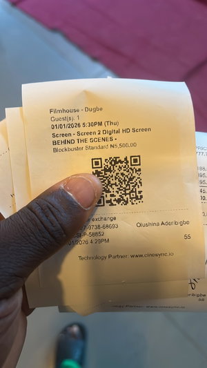 Dark-skinned hand holding cinema receipt, green shoes.