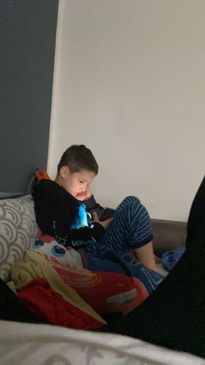 Boy in hoodie and striped pajamas on bed with tablet