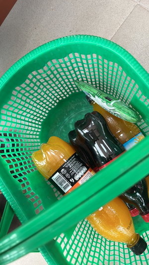 Green basket with soda bottles on tiled floor.