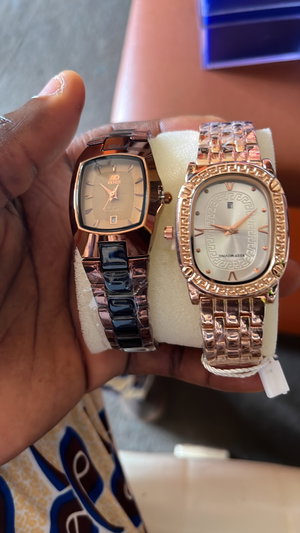 Dark-skinned hands holding two luxury watches on cushions.