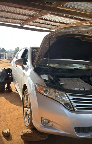 Man in gray shirt fixing silver car outdoors.