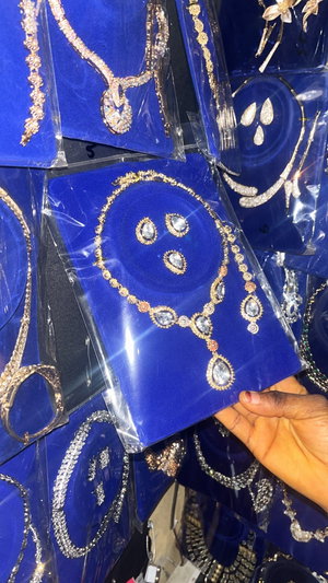 Hand holding gold crystal necklace display on blue trays.